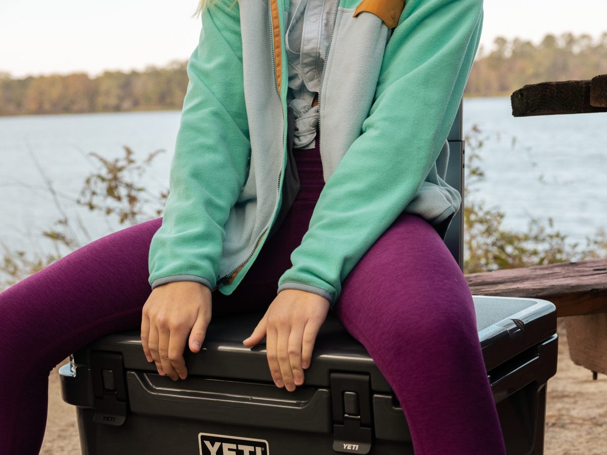 A woman sits on a black cooler.