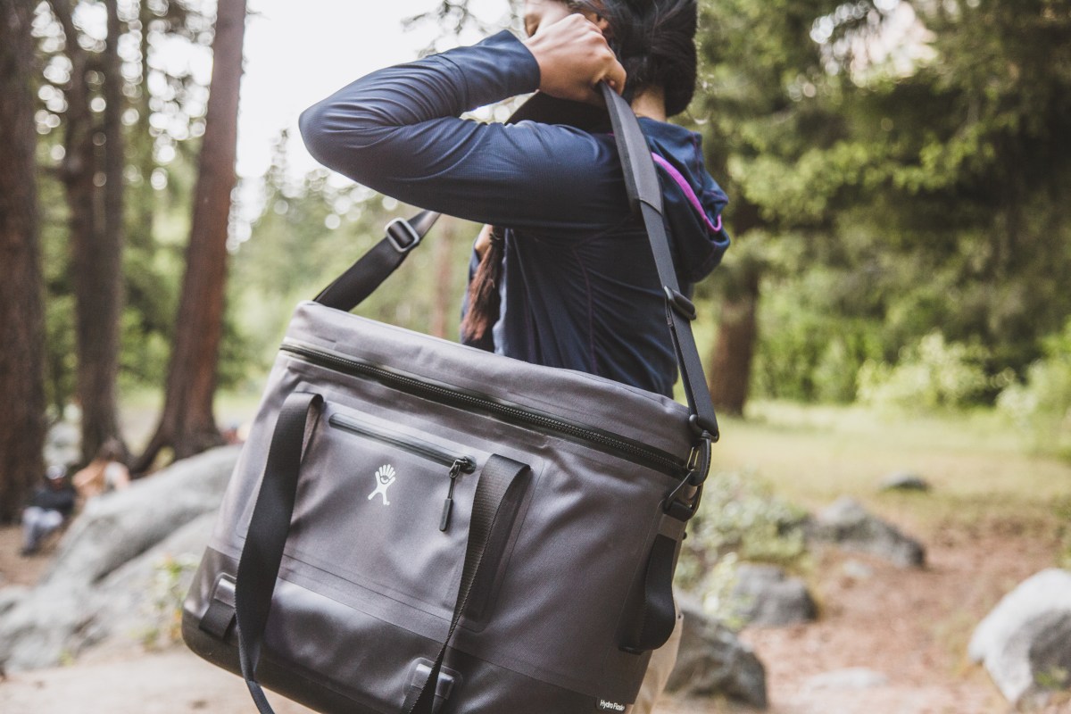 A woman hoists a soft cooler over her shoulder.