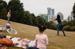 A group of people spend time at the park. Two of the people are throwing a frisbee.