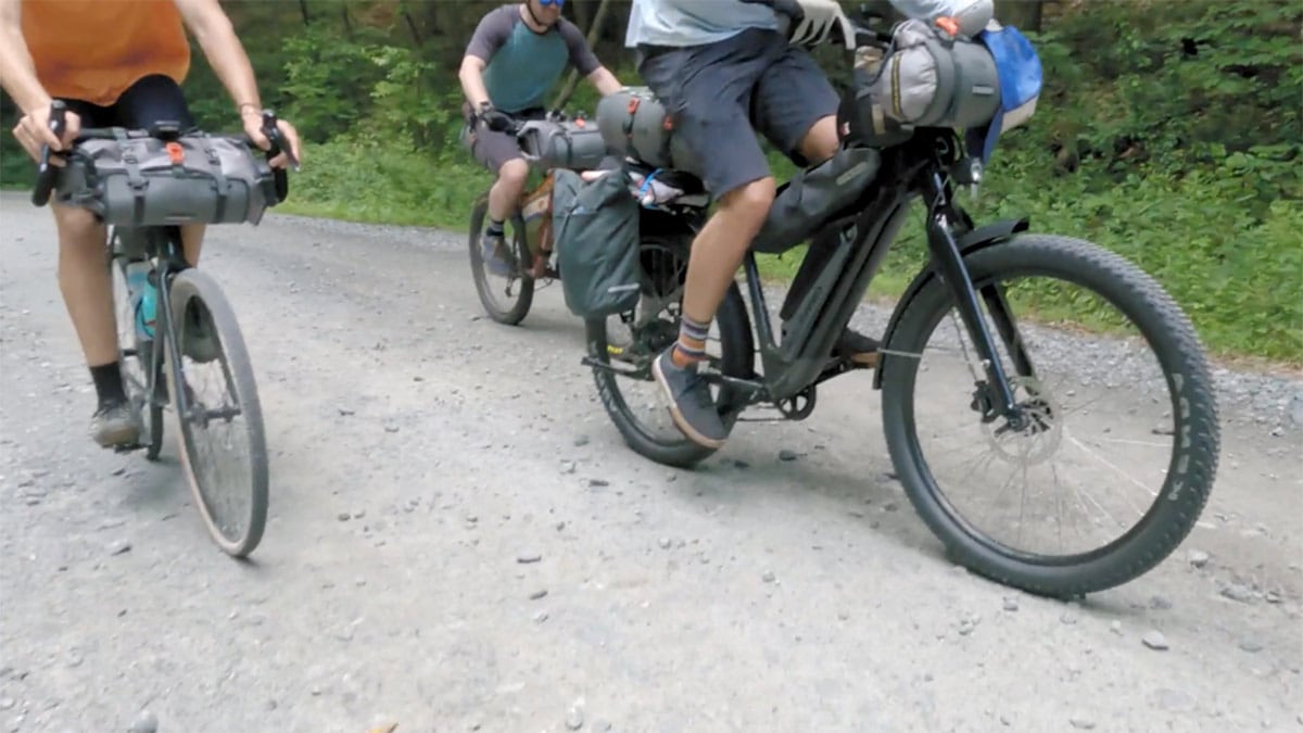 Three cyclists pedal down a gravel road.