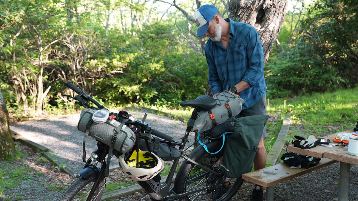 A person at a campground packs up bike bags on his electric bike, ready for the next route of a bikepacking trip.