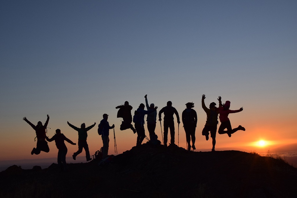 Hikers jumping at the top of a mountain at sunset.
