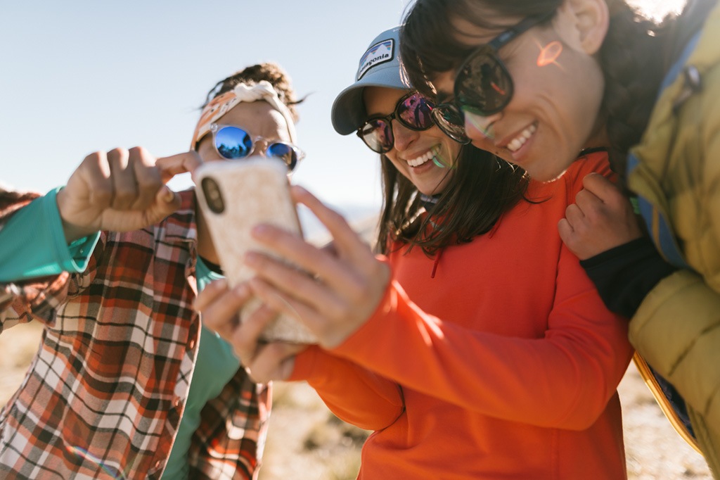 Three smiling people look at a smartphone together.