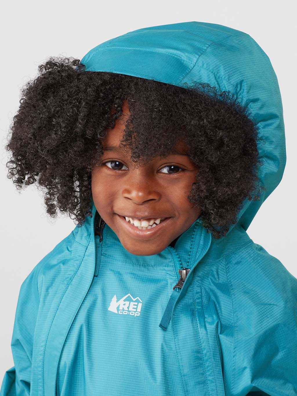 A smiling child is wearing a blue REI Co-op Rainwall Rain Jacket