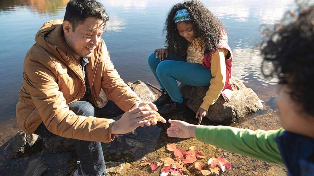 An adult and two children sit outside examining a fall leaf together
