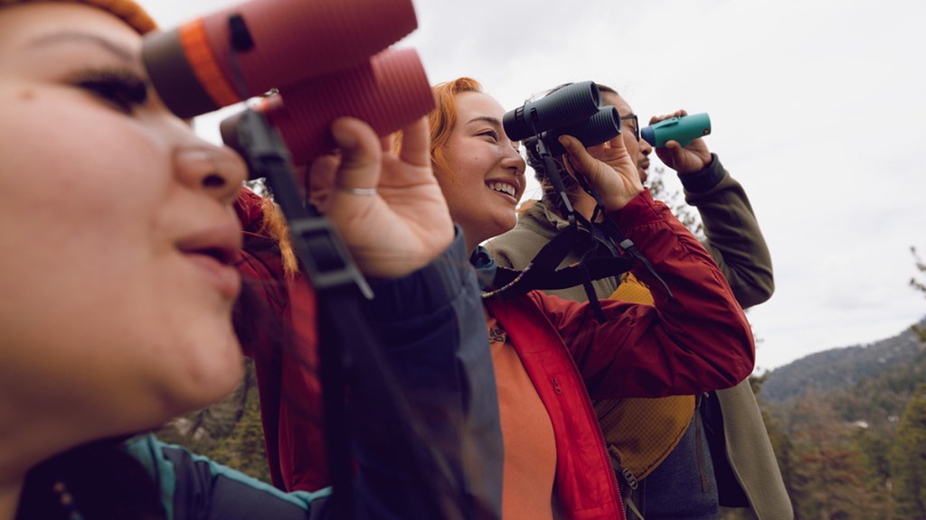 Three people peering through binoculars and smiling.