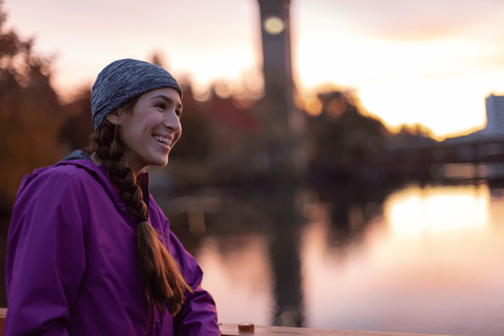 A person wearing a hat standing in front of a waterfront scene at sunset