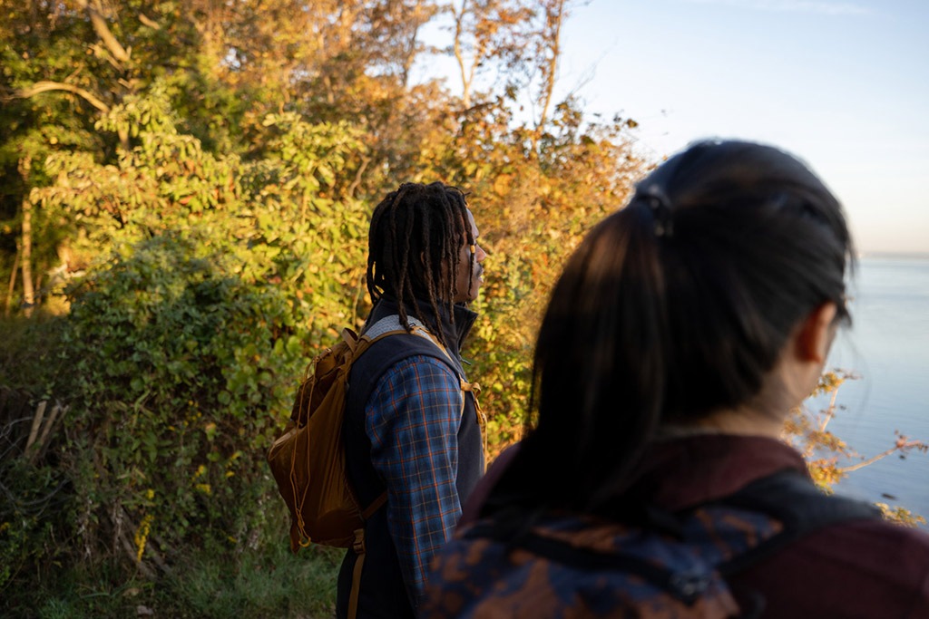 Two people on a hike in front of trees turning yellow and orange.