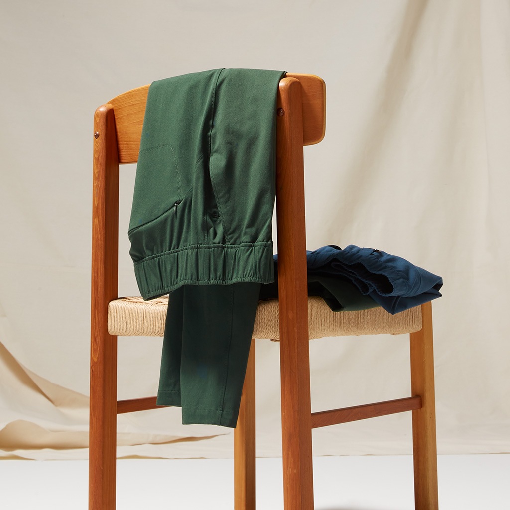 A pair of athletic pants laid on the back of a wooden chair against a cloth backdrop.