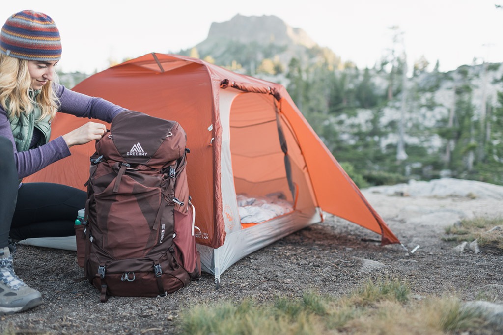 A camper packing a pack next to a tent