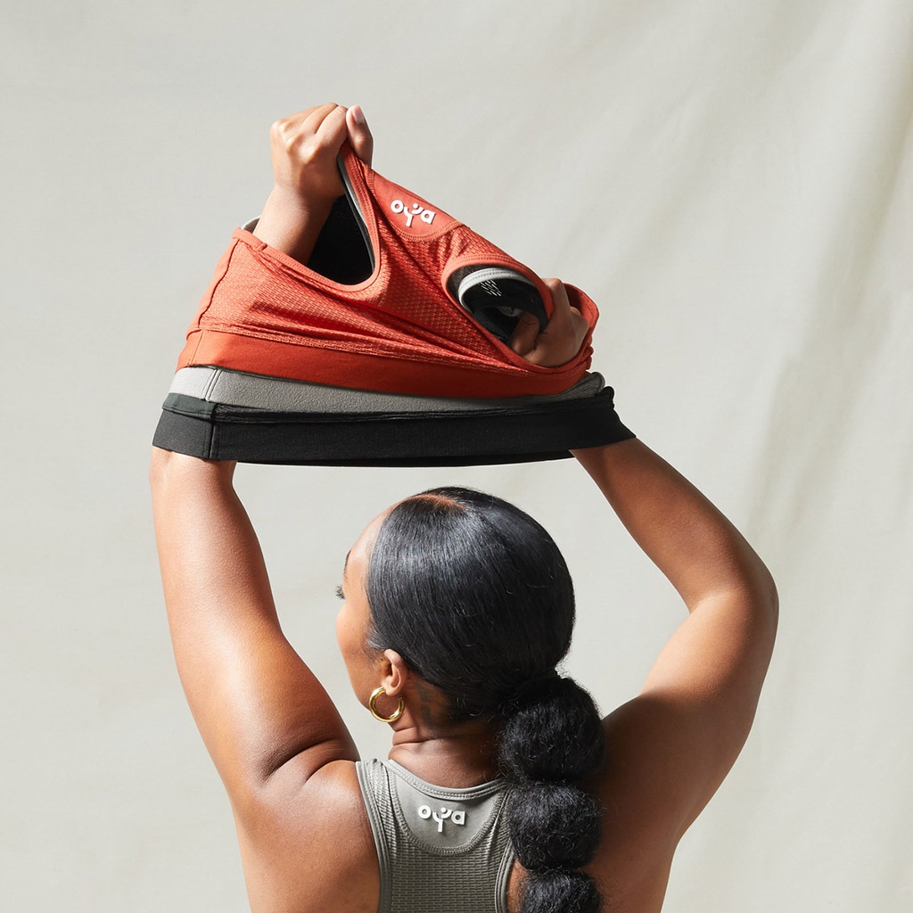 A woman stretching up with sports bras in her arms.