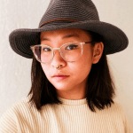 A portrait of writer Holly Yu Tung Chen wearing a brimmed hat, glasses and a cream-color sweater.