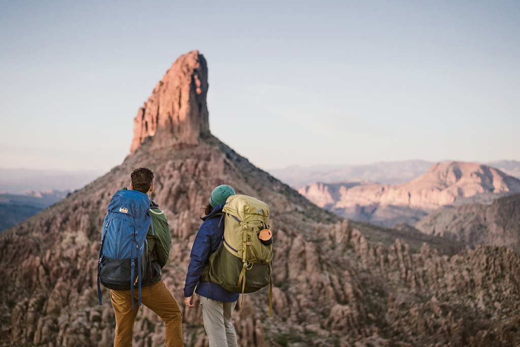 Two people with hiking packs on stand looking off at a geological formation in the distance.
