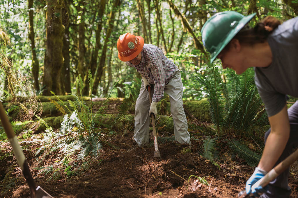 Two people repair a trail wearing WTA hardhats.