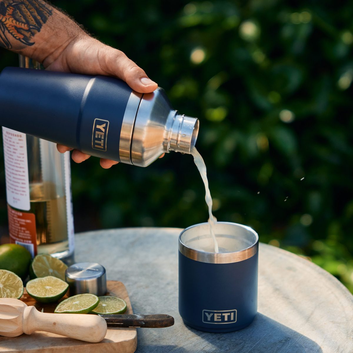 A person pours a cocktail from a YETI shaker into a camp cup.