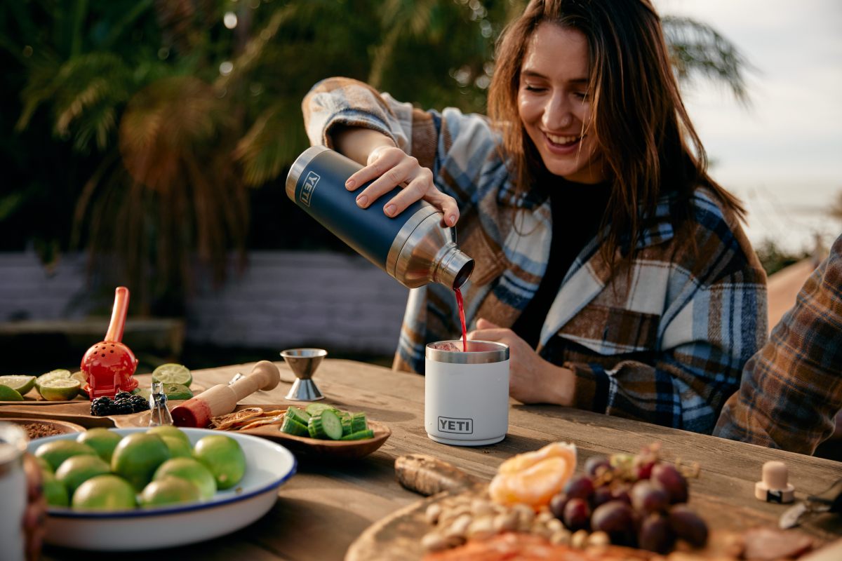 A woman pours a cocktail from a shaker into a camp cup. 