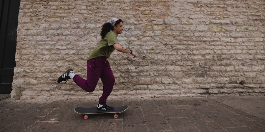 Eine Person beim Skateboarden in einem olivgrünen T-Shirt und burgunderroten Jogginghosen aus der REI Co-op Active Pursuits-Kollektion