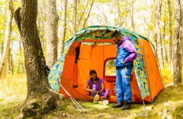 Two people wearing colorful Outdoor Afro + REI Co-op clothes stand in front of a brightly colored tent with a patterned fly designed by Chelsea Alexander