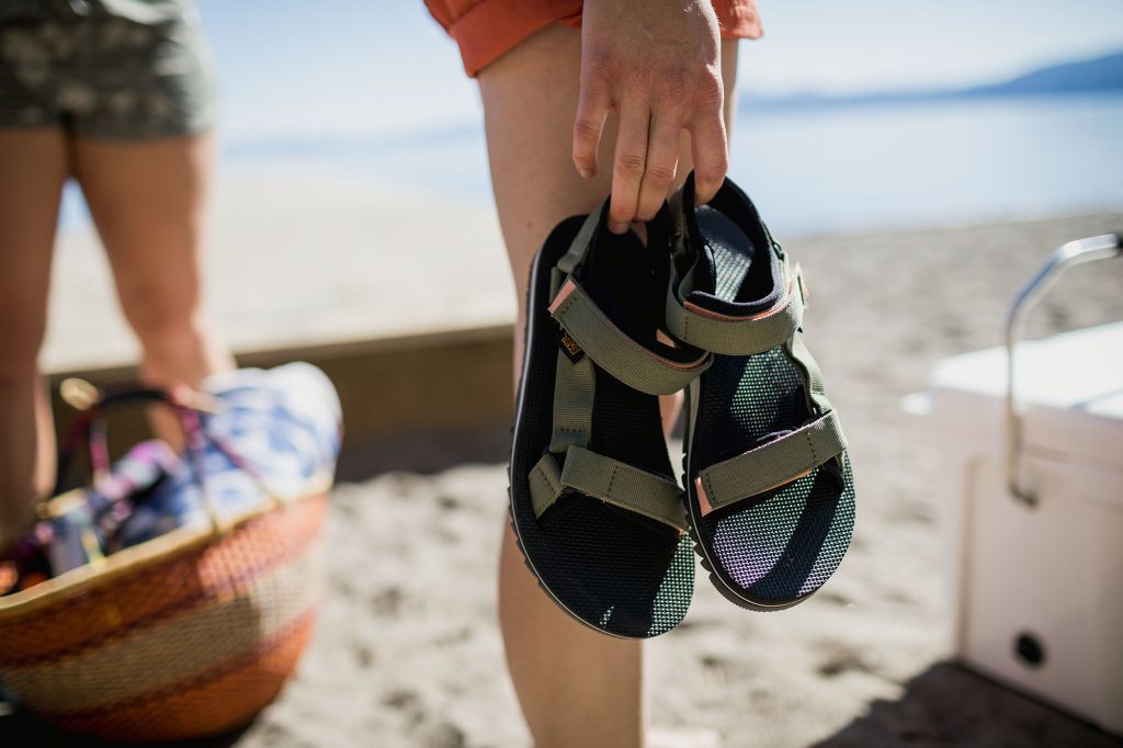 A person walking on the beach carries their Teva Original Universal Sandals