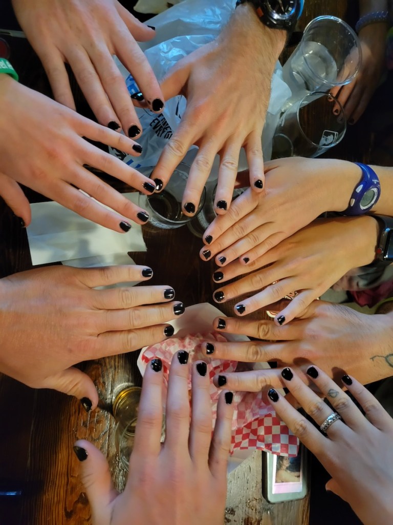 Multiple hands in a circle with black nail polish.