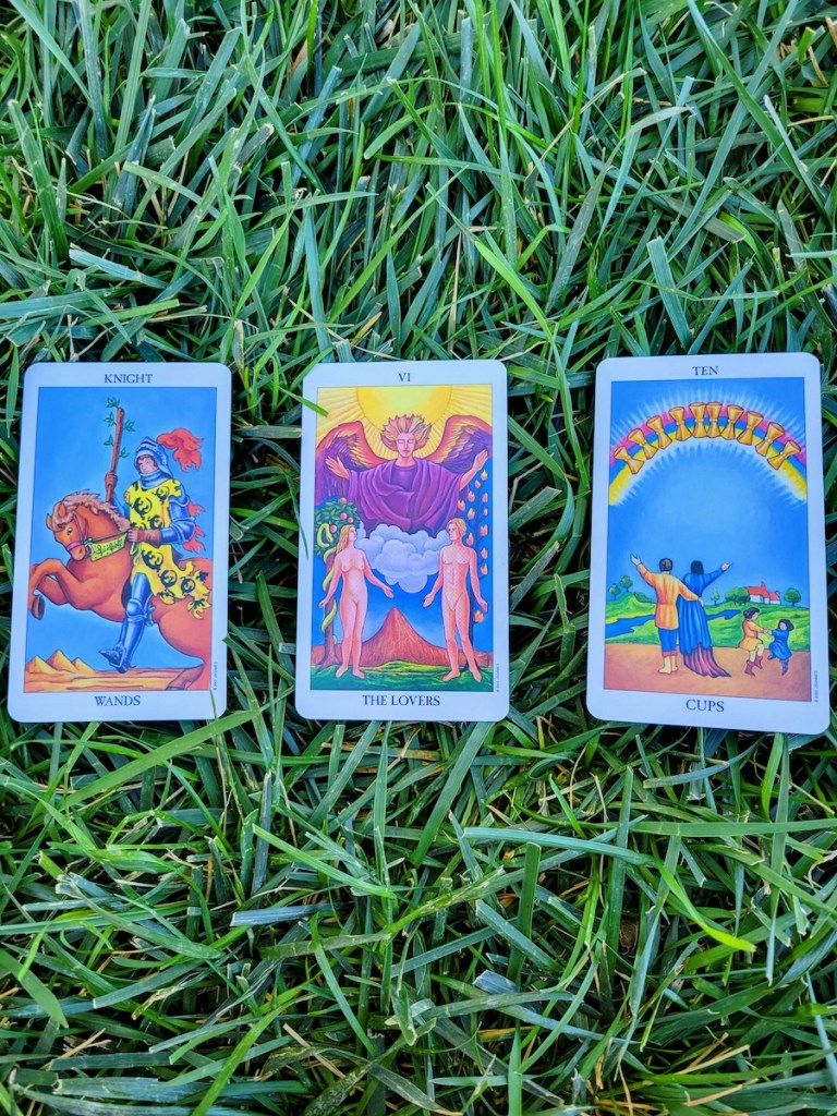 Three colorful tarot cards arranged on grass.