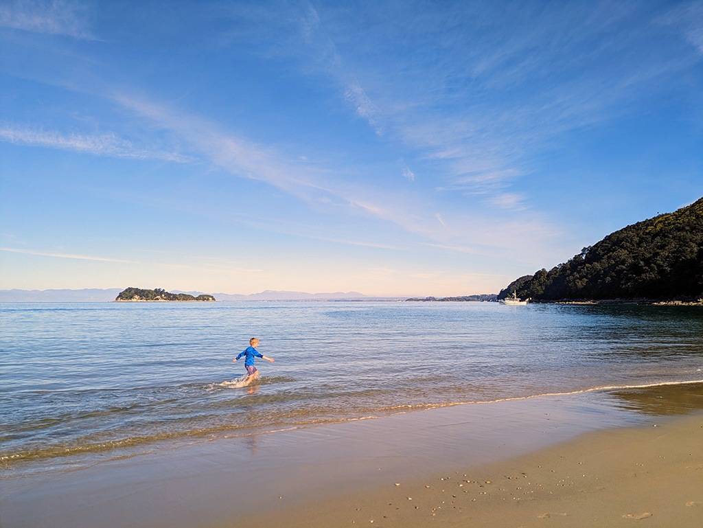 A young person runs into the shallow water along an ocean beach.