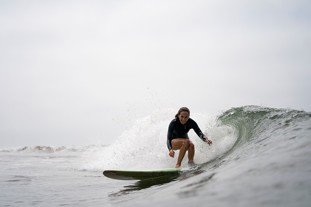 A person on a surfboard catching a wave smiles at the camera.
