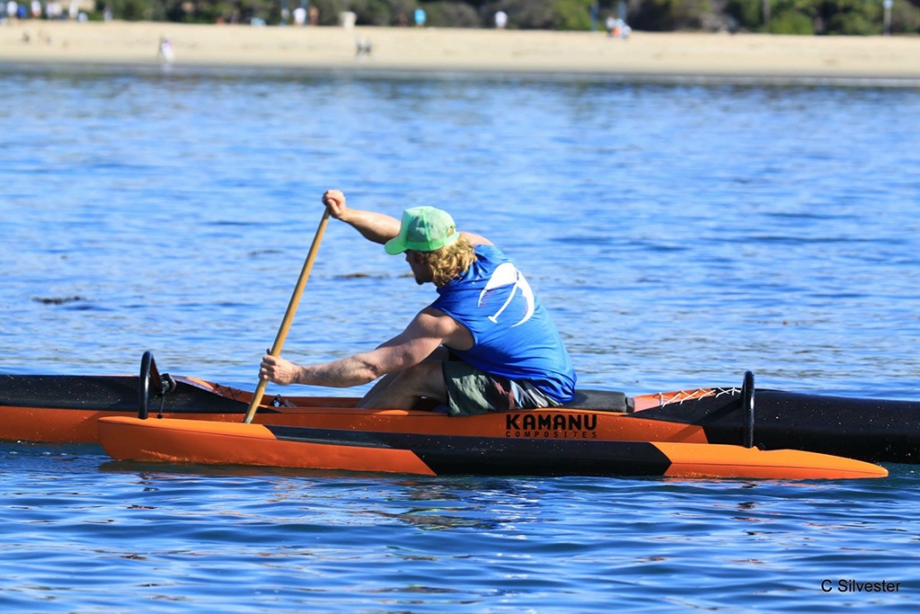 A person in a blue shirt and green hat sits in a boat and paddles in the water.
