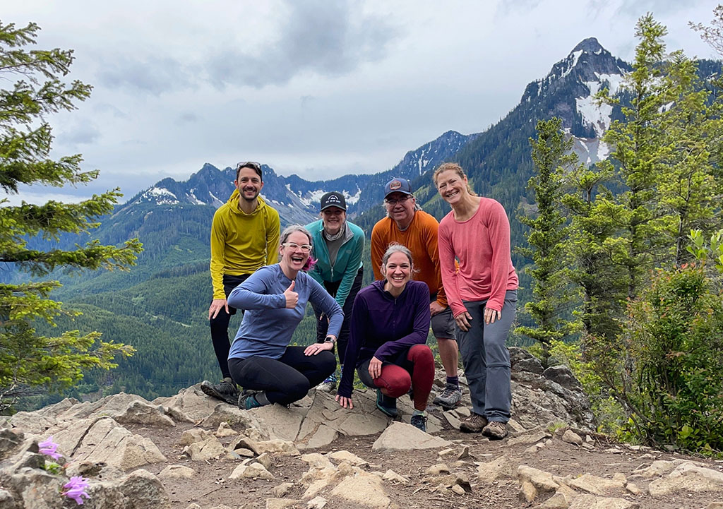 A group of people in brightly colored tops stand on a peak and take a group picture.