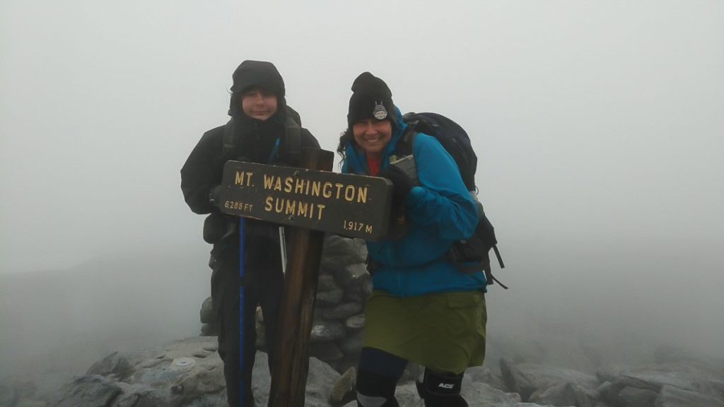 Two hikers huddle at the Mt. Washington Summit marker on the AT