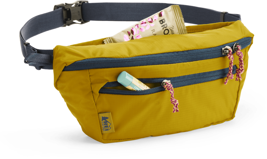 A green waist pack with a lip gloss and an energy bar coming out of two of the pouches.