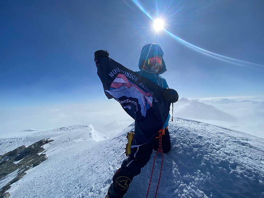 Erin Parisi stands at the summit of a mountain holding her Transcending flag.