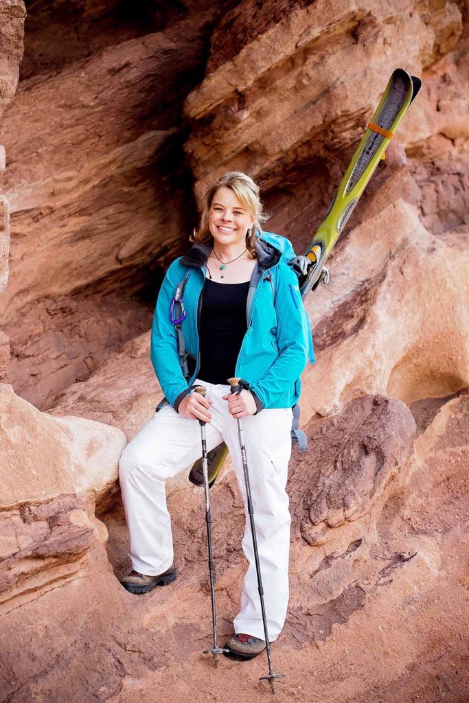 Erin Parisi standing on red rocks holding trekking poles.