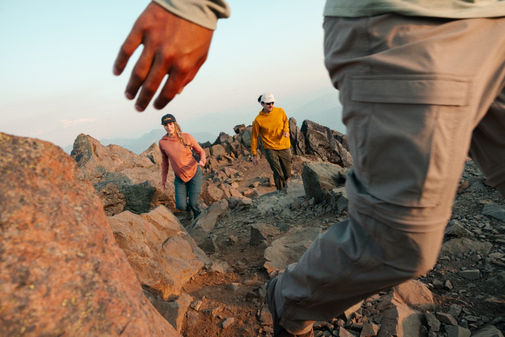 Three people are hiking; one is passing close to the camera and is only seen in partial view