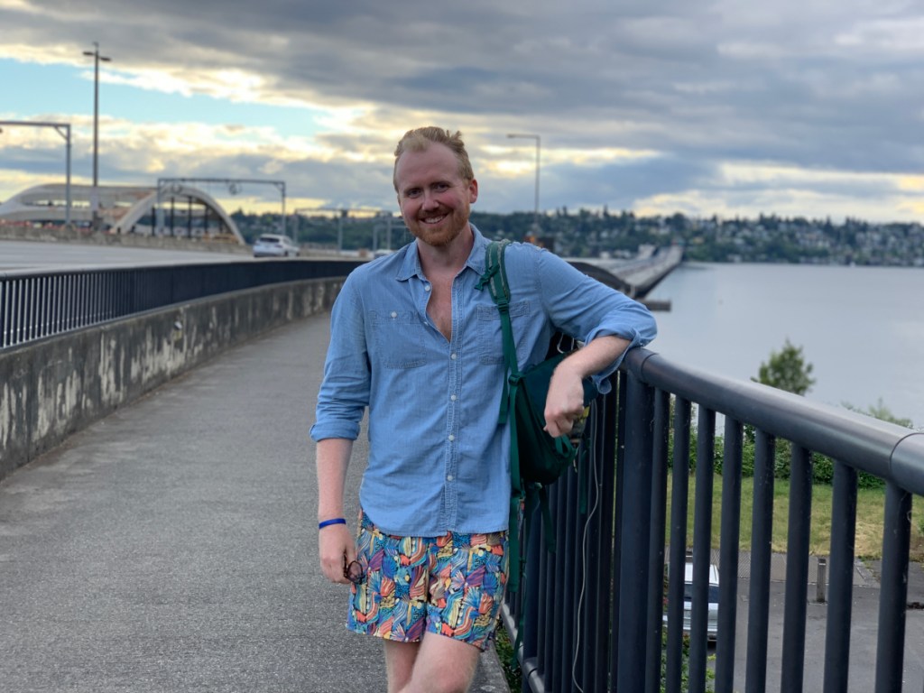 A person leans against the railing of a bridge and smiles