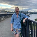 A person leans against the railing of a bridge and smiles