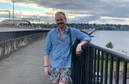 A person leans against the railing of a bridge and smiles