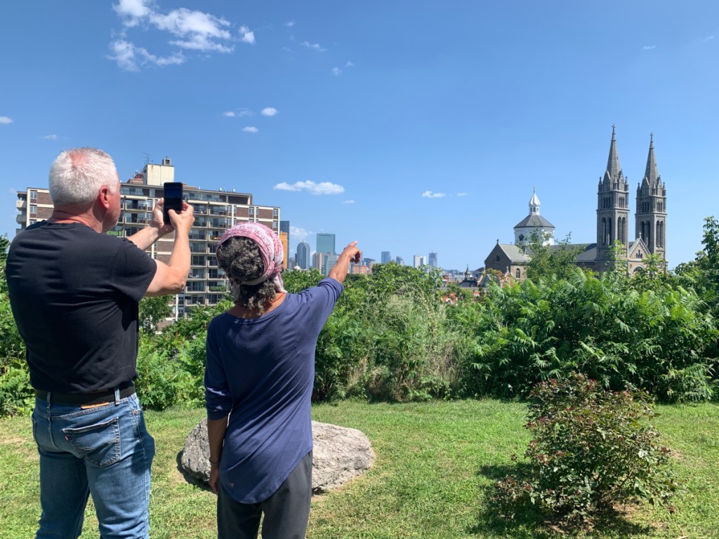 Two people stand in front of a green space with an urban view