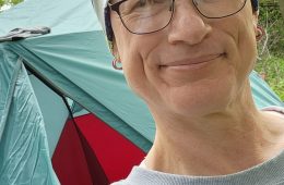 A person wearing a hat takes a selfie in front of an REI Co-op tent