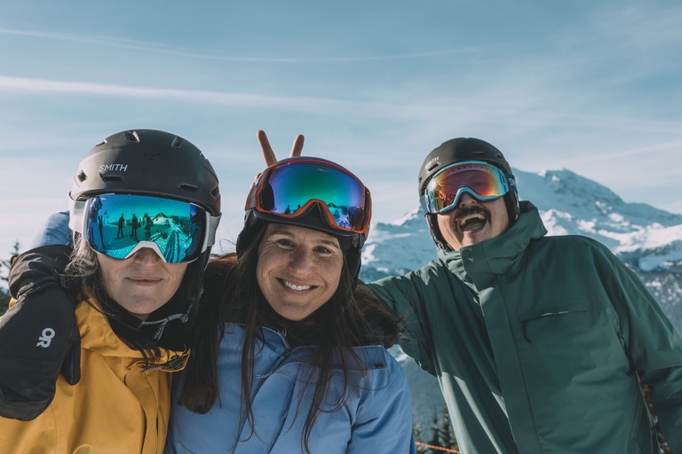 Three skiers wearing REI Powderbound ski jackets post in front of a mountain