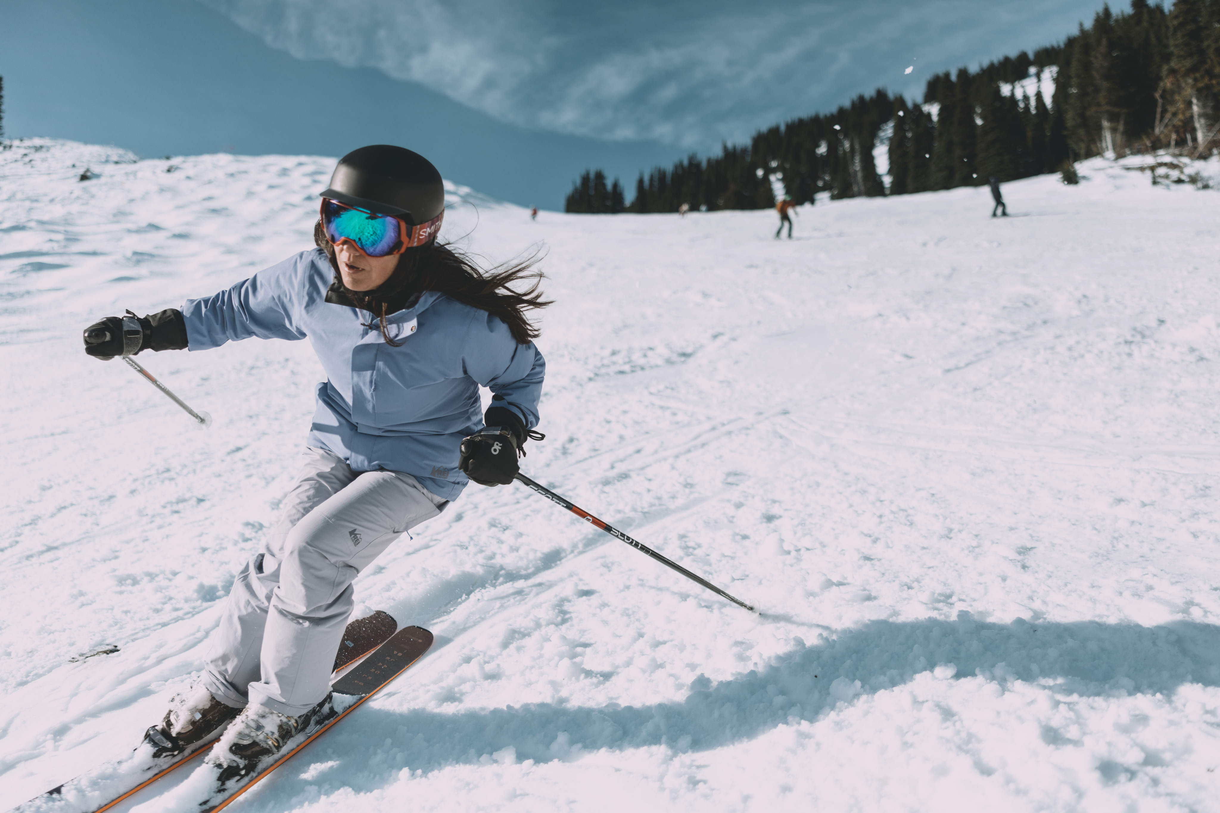 A skier wearing a blue ski jacket cruising down the slope