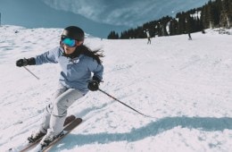 A skier wearing a blue ski jacket cruising down the slope
