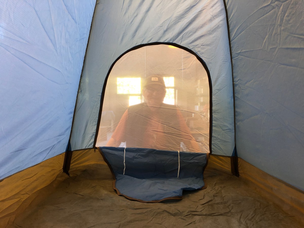 A view from inside a tent looking out toward the front door where a person peers in.