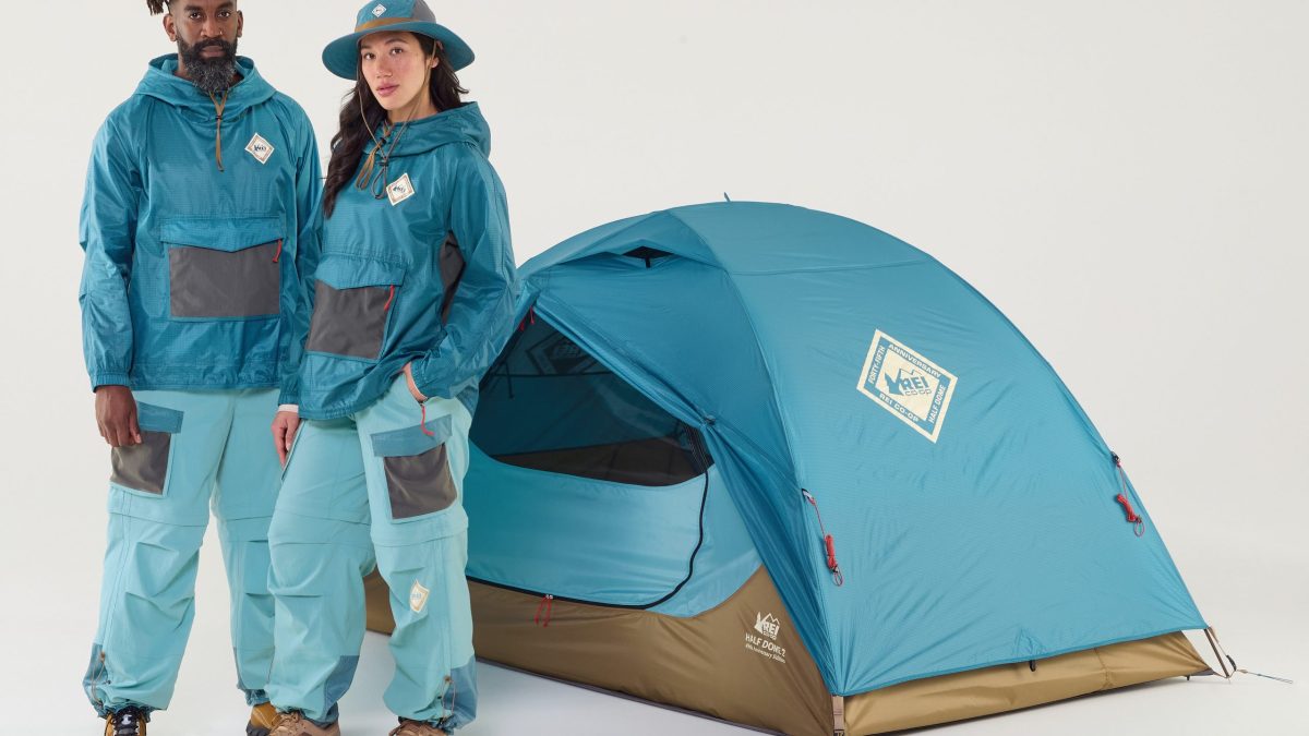 Two people wearing blue outfits stand in front of the 45th Anniversary edition of the REI Co-op Half Dome tent.