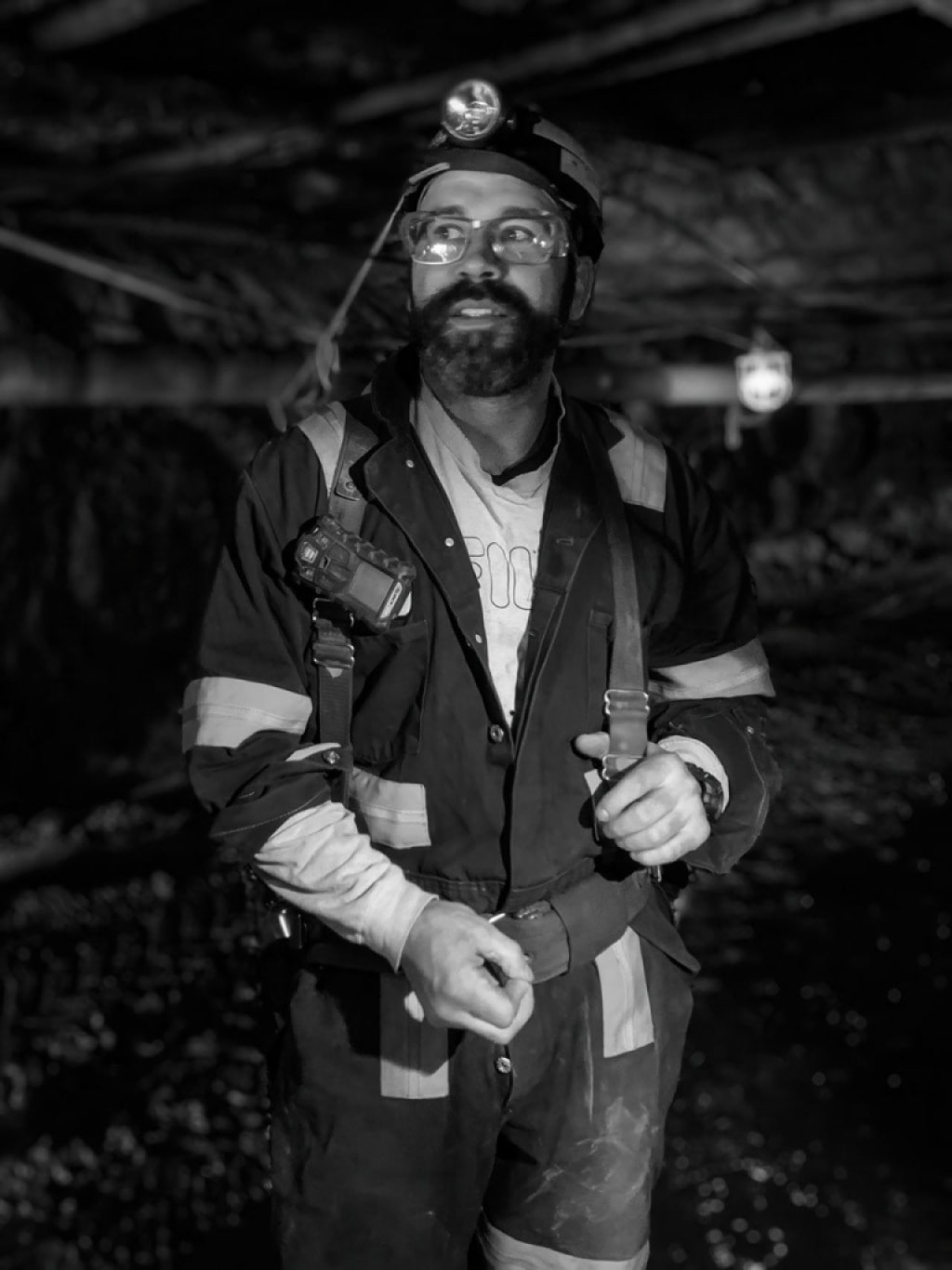 A person wearing a mining uniform including a headlamp and safety gear, in a moine