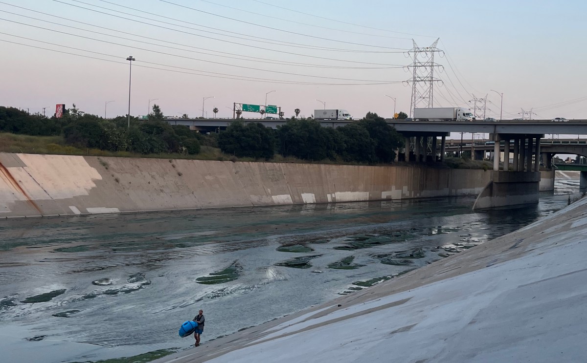 The LA River in the evening, with a person carrying a blue packraft up from the river.