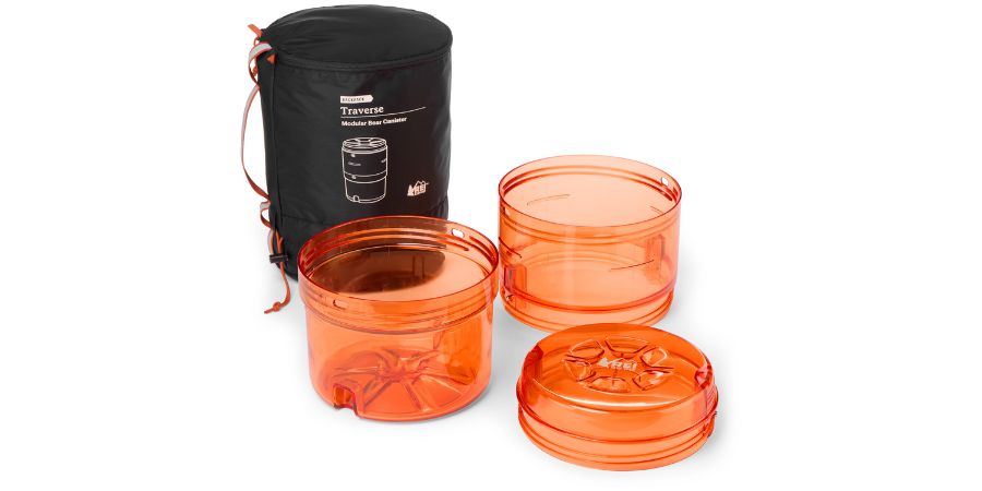 An orange three-part bear canister is disassembled and displayed along with its carrying sack.