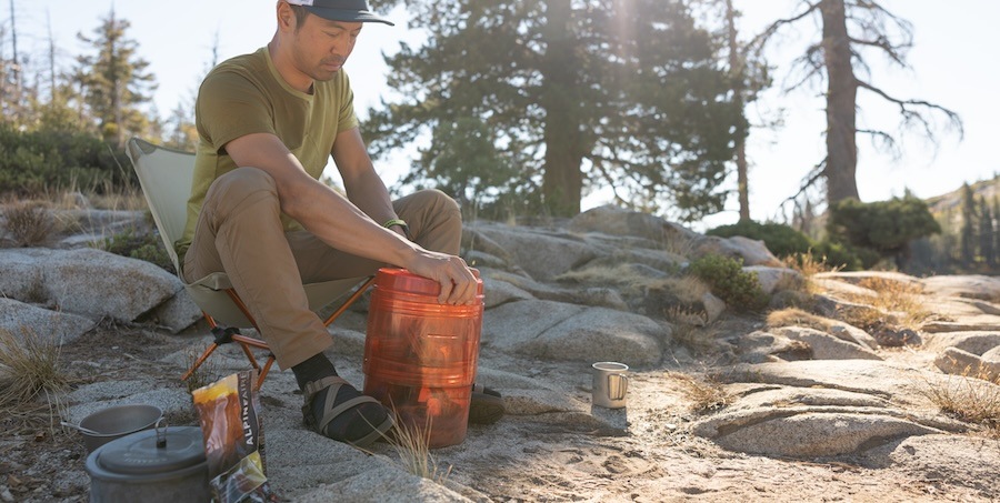 A camper opens a transparent orange bear canister.