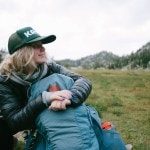 A person sits with a backpack in a mountain setting
