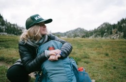 A person sits with a backpack in a mountain setting